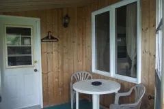 A small table and two chairs are set up on the covered porch of the cabin.