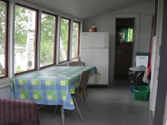 The veranda of cottage 3 includes a dining table and a refrigerator with a view of the forest.