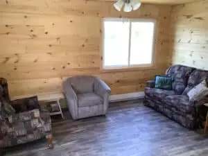 The living room of cabin 2 includes a sofa, an armchair, and natural wood walls.