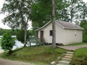 Exterior view of cabin 6, located near the shoreline and surrounded by trees.