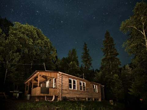 Vue nocturne du chalet en bois rond sous un ciel étoilé.