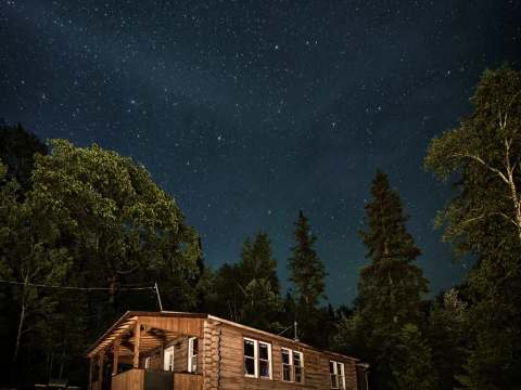 Le chalet en bois rond est illuminé sous un ciel étoilé durant la nuit.