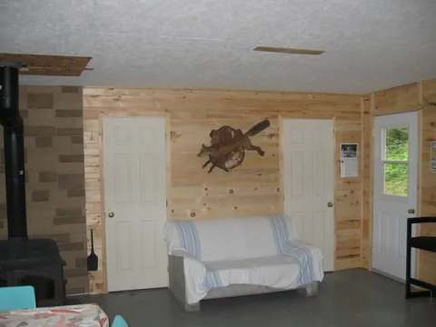 Vue de l'intérieur du chalet avec son coin salon, son poêle à bois et ses murs en bois naturel.