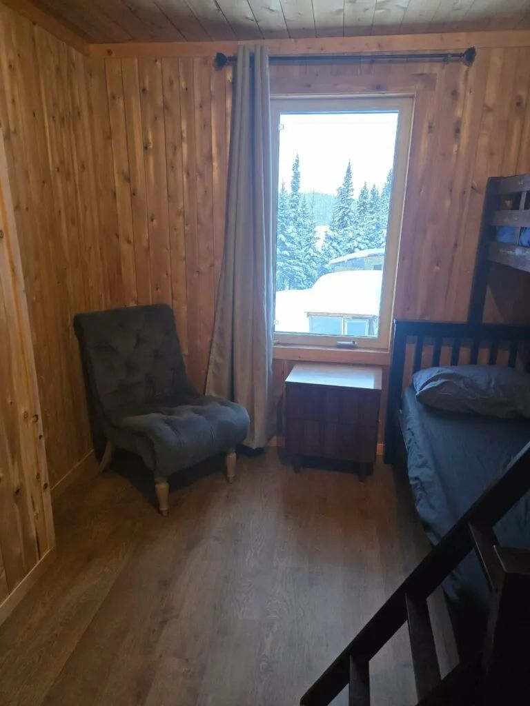 Une chambre confortable avec un lit superposé, un fauteuil et une vue sur la forêt enneigée.
