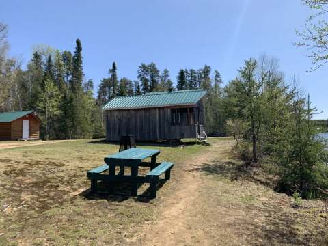 Vue extérieure d'un camp rustique avec sa table de pique-nique au bord de l'eau.