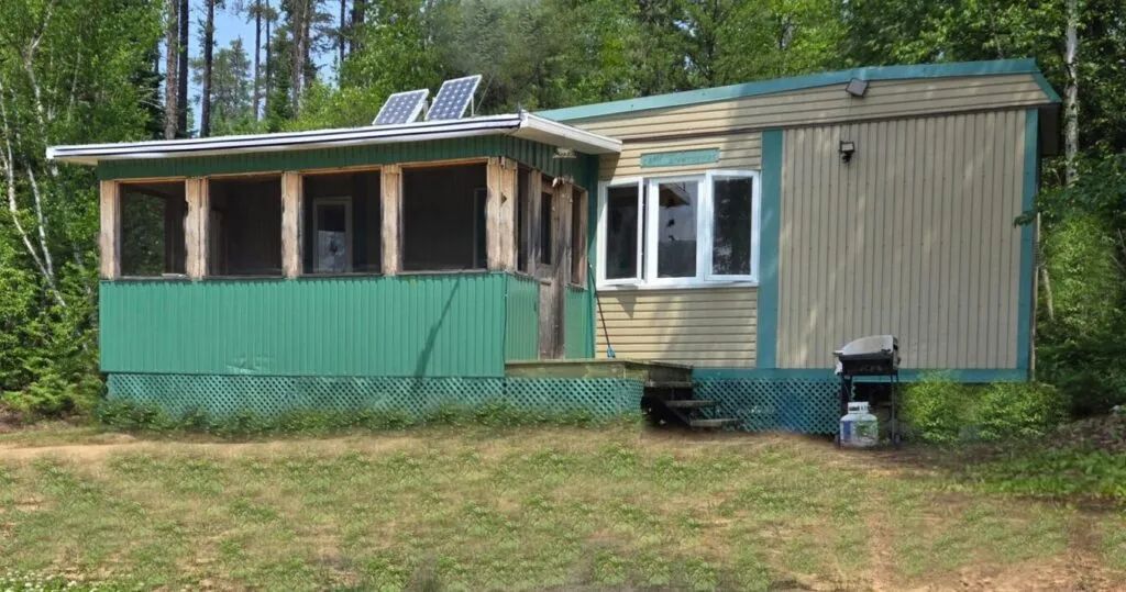 Exterior view of the cabin featuring a screened-in porch and solar panels on the roof.