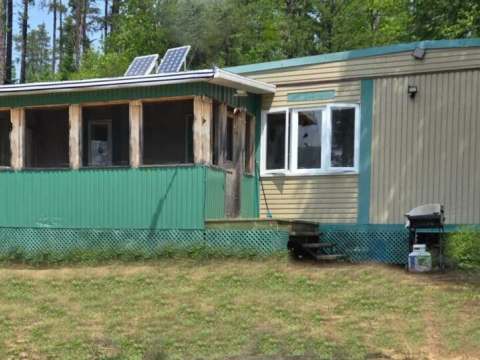 Exterior view of the cabin featuring a screened-in porch and solar panels on the roof.