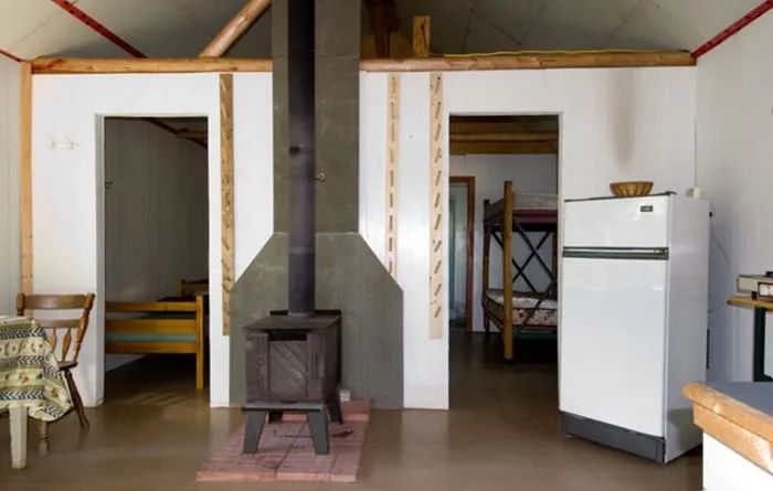 Interior view of the rustic cottage featuring a wood stove, a refrigerator, and beds.