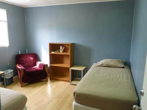 Cette chambre fonctionnelle comprend deux lits simples, un fauteuil et des espaces de rangement.