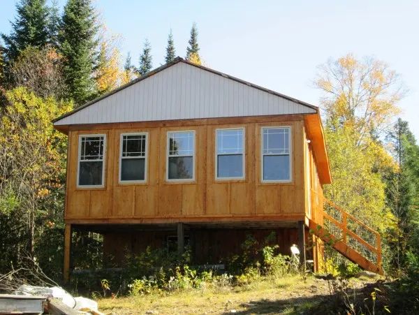 Le Camp Lac Trap est un chalet en bois sur pilotis entouré d'arbres.