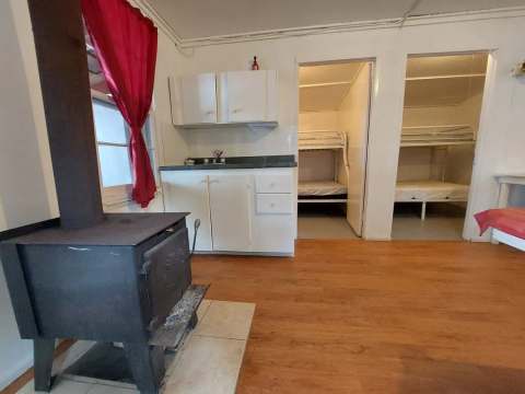 Vue de l'intérieur du chalet comprenant un poêle à bois, un coin cuisine et des chambres avec lits superposés.