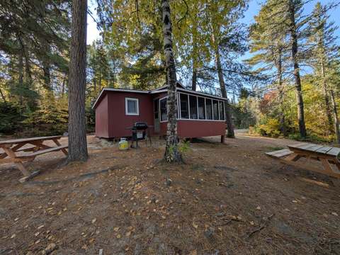 Exterior view of cabin 5 surrounded by trees with picnic tables and an outdoor barbecue.