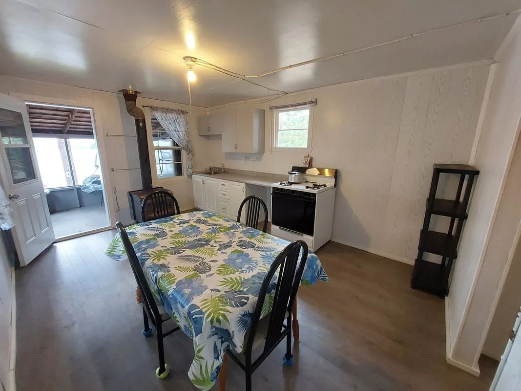 Vue sur la cuisine et la salle à manger du chalet avec poêle à bois et porte donnant sur la véranda.