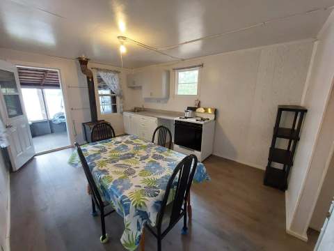 Vue sur la cuisine et la salle à manger du chalet avec poêle à bois et porte donnant sur la véranda.