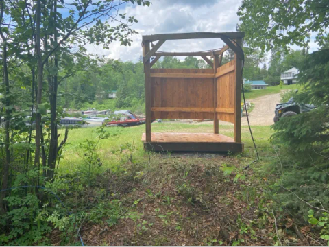 An outdoor wooden shower structure is set up on the camping site.