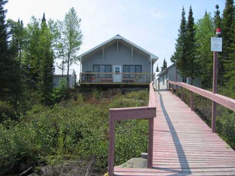 Vue du chalet principal avec sa grande galerie, accessible par une rampe d'accès en bois.