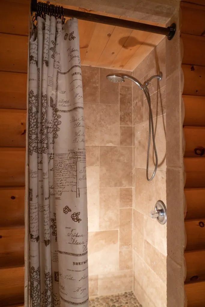 Cette douche est aménagée avec des parois en céramique au sein d'une structure en bois rond.