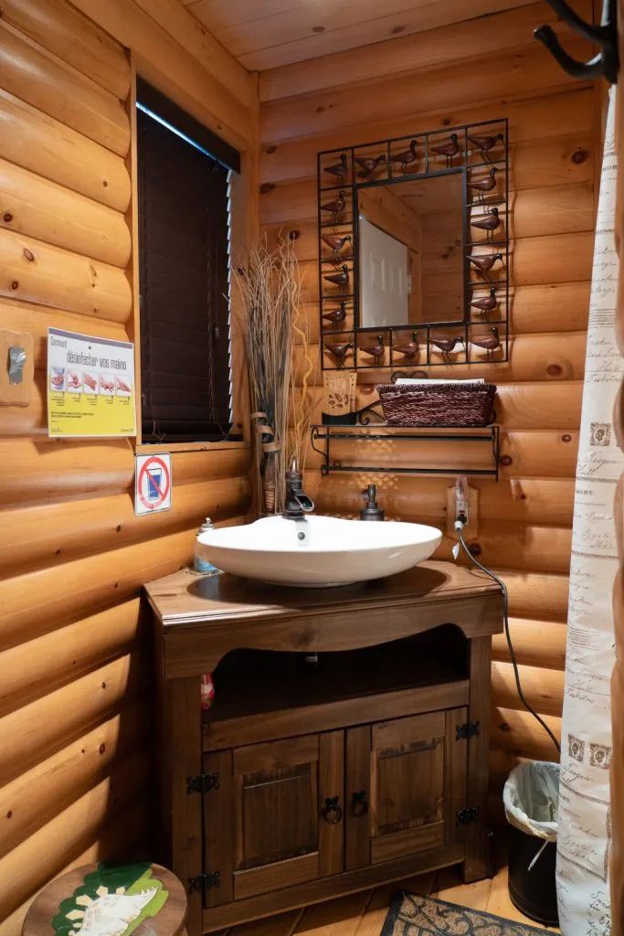 Vue de la salle de bain en bois rond avec lavabo vasque et miroir décoratif.