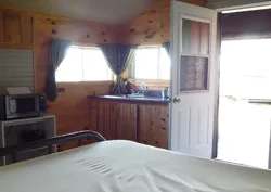 Vue intérieure du chalet comprenant un lit, une kitchenette et une porte donnant vers l'extérieur.