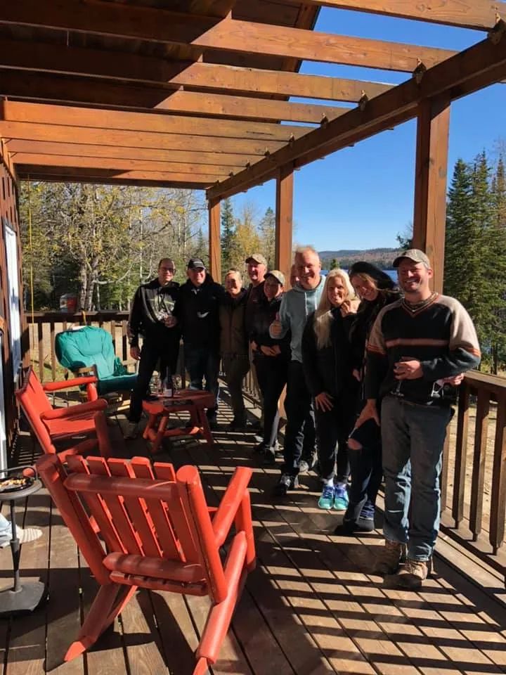 A group enjoys the covered cottage deck with a view of the forest and the lake.