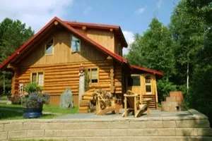 Vue extérieure du chalet en bois rond avec terrasse et chaises de détente.