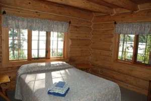 Vue intérieure de la chambre du chalet Dogwood avec ses murs en bois rond et sa vue sur l'extérieur.