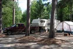 Emplacement de camping boisé accueillant un véhicule récréatif et une tente.