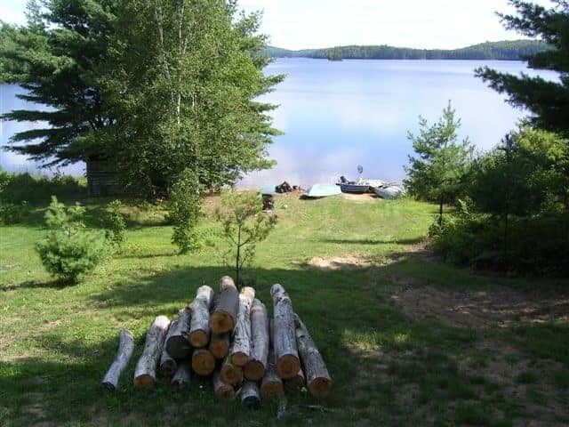View of the lake from the cottage grounds, including a woodpile and small boats.
