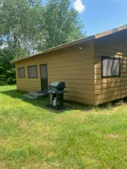Vue latérale du chalet avec son barbecue extérieur à disposition.