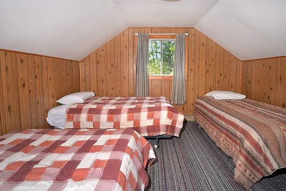 This attic bedroom features three single beds and wood paneled walls.