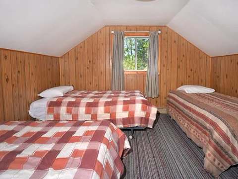 This attic bedroom features three single beds and wood paneled walls.