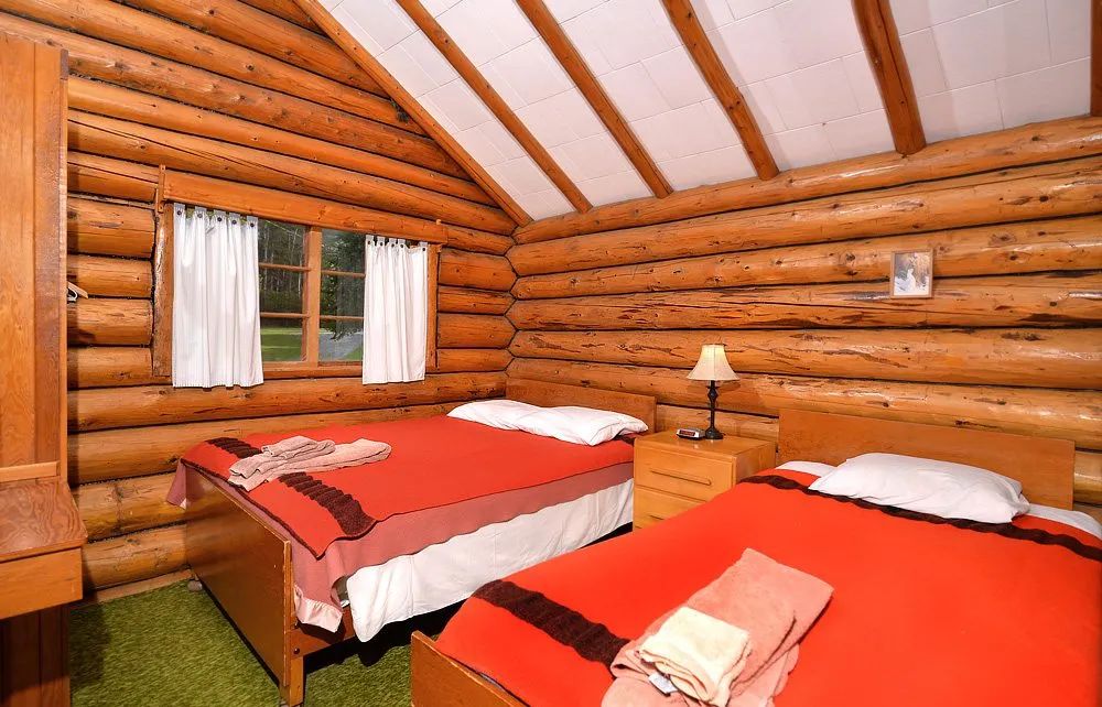 Cette chambre rustique en bois rond comprend deux lits simples avec une literie colorée.