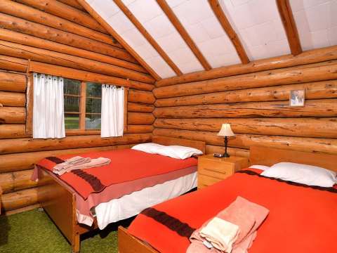 Cette chambre rustique en bois rond comprend deux lits simples avec une literie colorée.