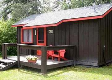 Vue latérale du chalet avec sa galerie en bois et ses deux chaises rouges.