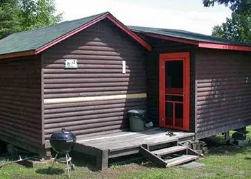 Vue extérieure du chalet en bois avec une galerie et un barbecue à l'entrée.