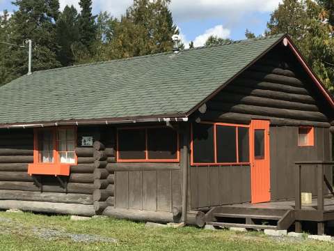Vue extérieure du chalet numéro 10 avec son revêtement en bois rond et ses accents orangés.