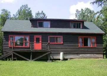 Vue extérieure de ce chalet en bois avec galerie et portes et fenêtres aux accents rouges.