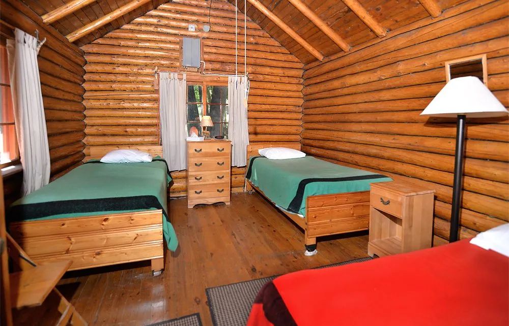 This rustic bedroom is furnished with three single beds and log walls.