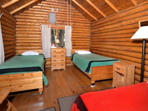 This rustic bedroom is furnished with three single beds and log walls.