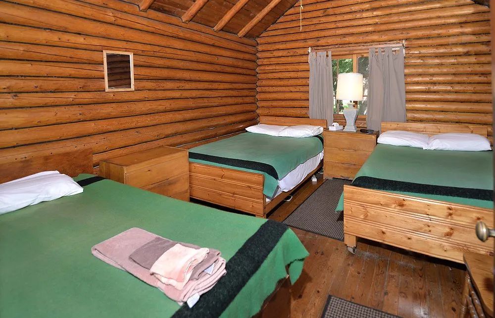 This rustic cabin bedroom features three beds with green blankets.