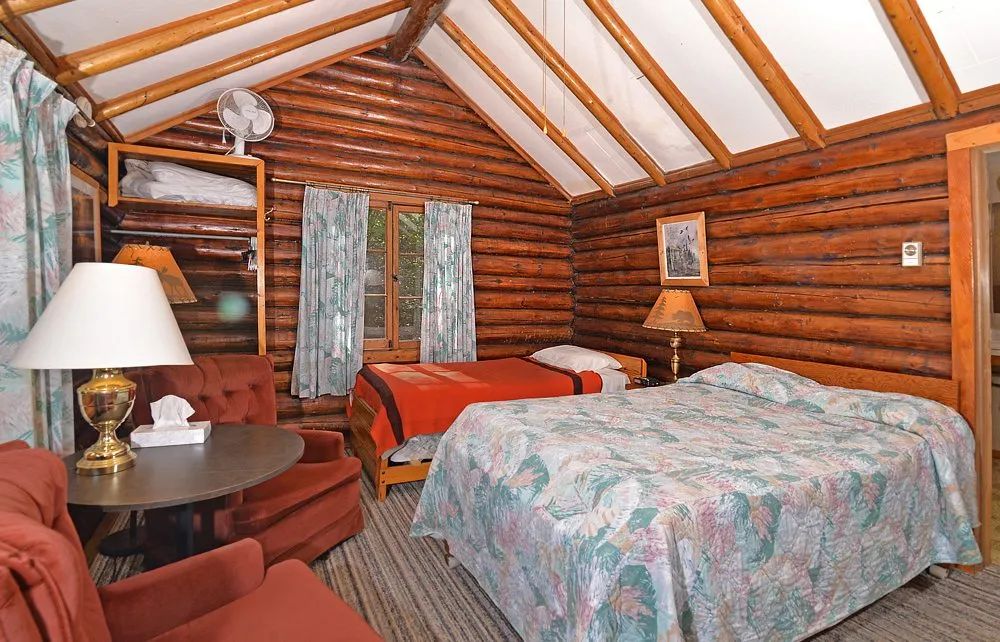 This rustic log cabin bedroom features two beds and a seating area with a table.