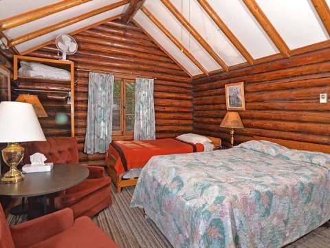 This rustic log cabin bedroom features two beds and a seating area with a table.