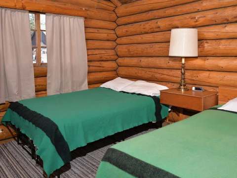 La chambre du chalet 9 dispose de deux lits avec une table de chevet et des murs en bois rond.