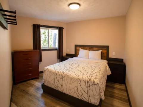 This bedroom features a double bed, a wooden dresser, and a window overlooking the outdoors.