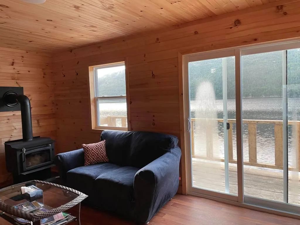 The cabin living room offers a view of the lake and a wood stove for your comfort.