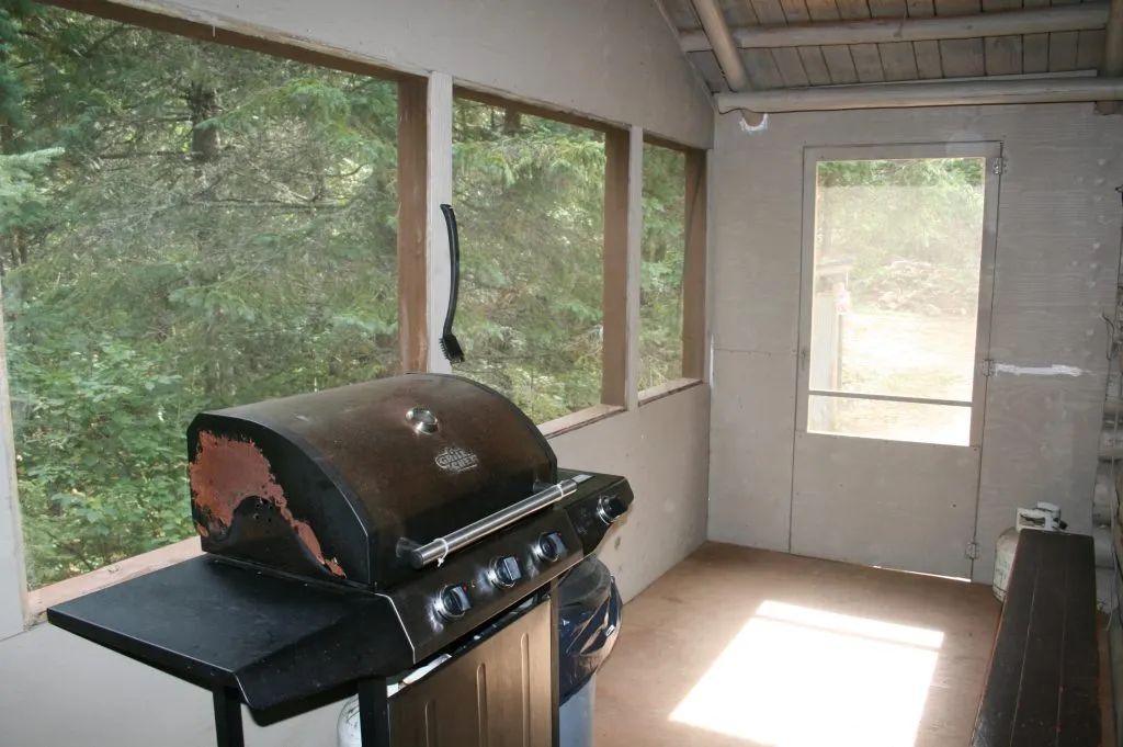 Une véranda grillagée équipée d'un barbecue pour cuisiner en profitant de la vue sur la forêt.