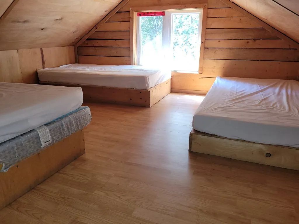 Cette chambre mansardée sous les combles comporte trois lits simples avec une fenêtre en bois.