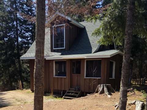 Le camp Farfadet est un chalet en bois situé en forêt avec une lucarne au niveau supérieur.
