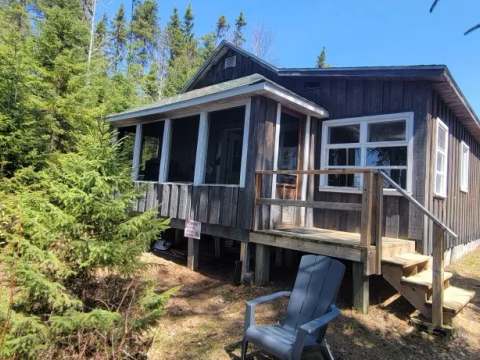 Le camp Refuge est un chalet en bois doté d'une galerie fermée, entouré par la forêt.