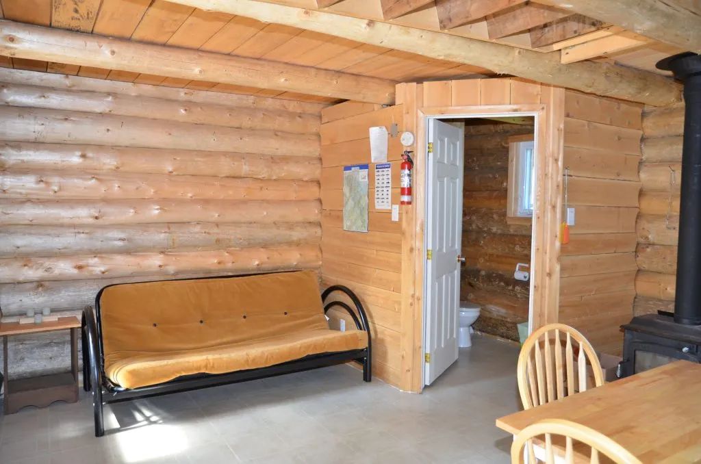 Vue intérieure du camp Refuge avec son coin salon, sa table et l'accès à la salle de bain.